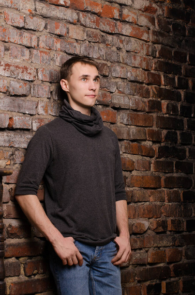 Portrait of a young man in a black jacket against the background of a brown, red and black brick wall - Photo, Image