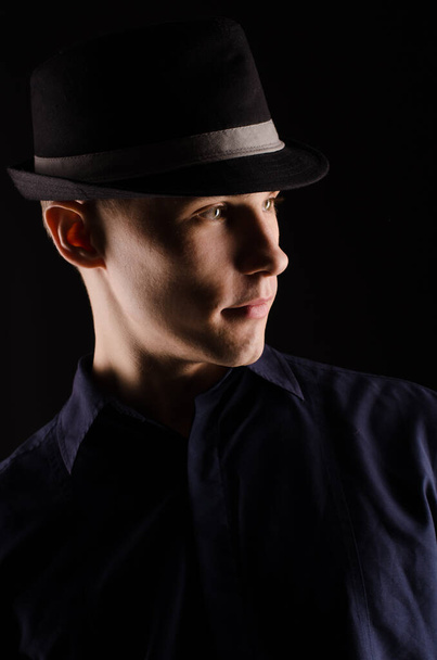 Portrait of a young man in a hat with a ribbon, close-up, on a black background, studio light - Фото, изображение