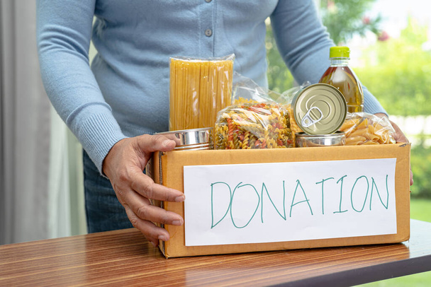 Добровольцы кладут различные сухие продукты в коробку для пожертвований для помощи людям. - Фото, изображение