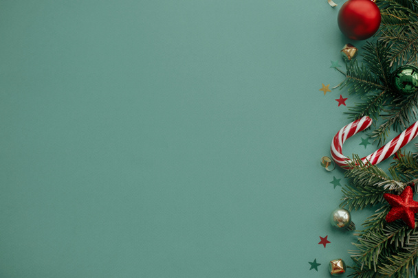 Καλά Χριστούγεννα! Κομψό χριστουγεννιάτικο σύνορο με εορταστικές διακοσμήσεις, κομφετί, κλαδιά ελάτης σε πράσινο φόντο. Χριστούγεννα επίπεδη lay, εποχές χαιρετισμούς πρότυπο κάρτα, χώρος για κείμενο - Φωτογραφία, εικόνα