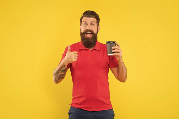 Excited man in casual red tshirt giving thumb holding disposable cup yellow background, paper-cup coffee. - Фото, зображення