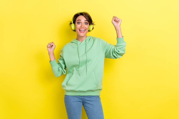 Photo of impressed overjoyed optimistic girl bob hairstyle wear green hoodie raise fists up yeah yell isolated on yellow color background. - Фото, изображение