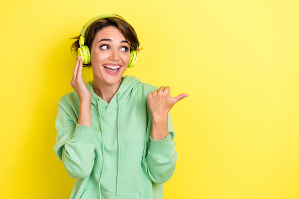 Portrait of good mood carefree nice woman with bob hairdo green hoodie directing look empty space isolated on yellow color background. - Foto, Imagem