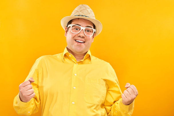 Portrait of Funny fat man tourist in hat and glasses emotionally rejoices and feels happiness isolated on yellow background, advertising banner - Fotografie, Obrázek