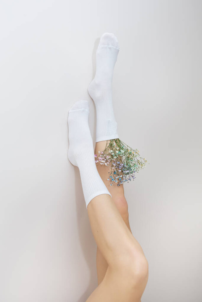 İçinde çiçekler olan beyaz çoraplı bir kızın bacakları dik duruyor. Pürüzsüz ve güzel bacaklar kavramı - Fotoğraf, Görsel