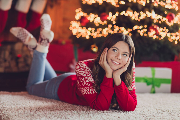 Photo of good mood satisfied girl with brunette hair wear red ornament jumper laying palms cheeks look empty space in house indoors. - Photo, image