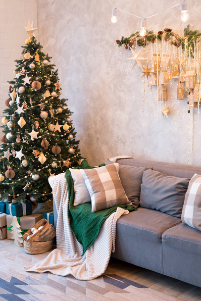 Εσωτερικό του σύγχρονου στούντιο σαλόνι με άνετο καναπέ διακοσμημένο με χριστουγεννιάτικα δέντρα και δώρα. Κάθετη εικόνα - Φωτογραφία, εικόνα