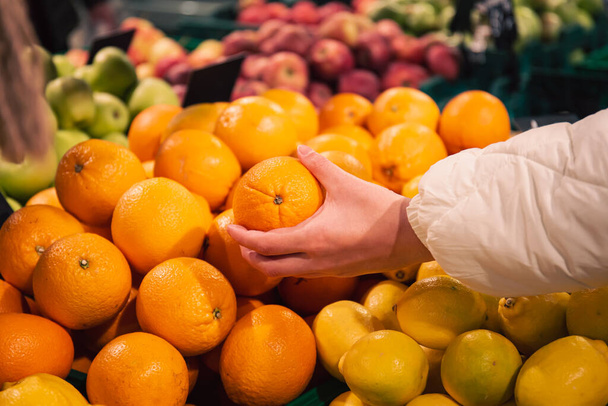 スーパーではオレンジを選ぶ女性が果物や野菜の通路でオレンジを拾います。女性ショッピングフード店. - 写真・画像
