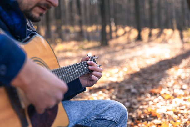 Primer plano, un hombre toca una guitarra acústica en el bosque durante la estación fría, copiar espacio. - Foto, imagen