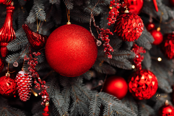 стильные рождественские украшения на елке, красивые игрушки, шары, конусы и огни в красных тонах. Рождественская уютная атмосфера в гостиной, Новый год. Праздничный дизайн интерьера - Фото, изображение