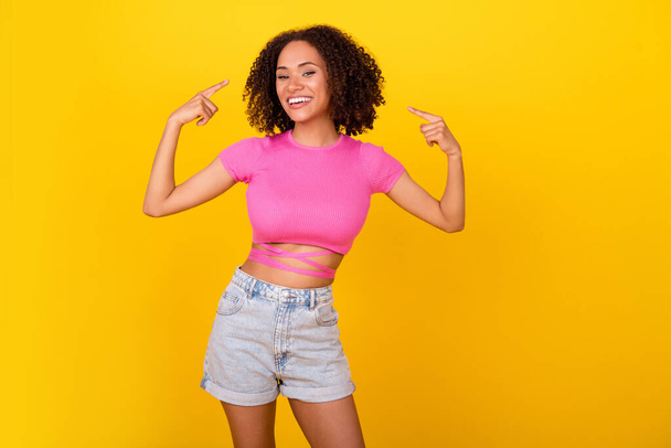 Photo of pretty positive girl point fingers self herself hair toothy smile isolated on yellow color background. - Foto, afbeelding
