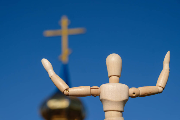 Una muñeca maniquí de madera con las manos extendidas sobre una iglesia y el fondo del cielo azul. Vista trasera. - Foto, imagen