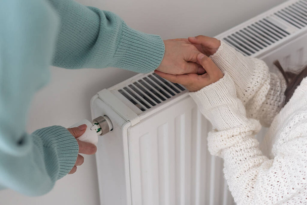 niño calentando manos en radiador de calefacción cerca de la pared blanca, primer plano. - Foto, Imagen