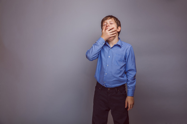 teenager boy yawns on gray background - Foto, afbeelding