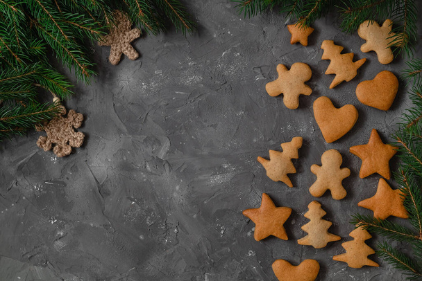 Composición navideña con galletas caseras de jengibre y ramas de abeto sobre un fondo gris. Galleta en forma de árbol de Navidad, hombre, estrella y corazón. - Foto, imagen