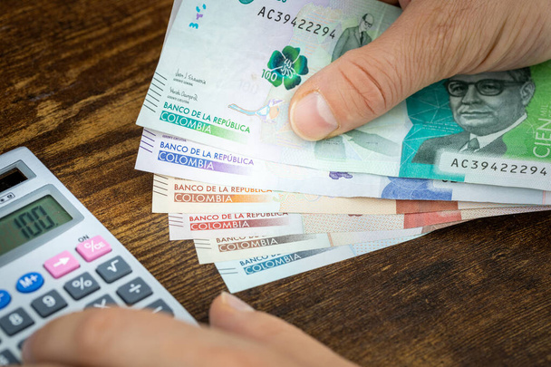 Homem tem pesos colombianos na mão e conta com calculadora de despesas ou ganhos, conceito financeiro, orçamento de casa dos colombianos - Foto, Imagem