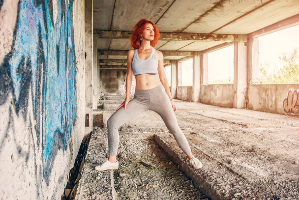 Фитнес-женщина в спортивной одежде делает упражнения на городской улице на сером бетонном фоне. - Фото, изображение