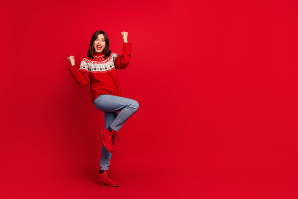 Full size photo of crazy satisfied girl raise fists shout yeah empty space isolated on red color background. - Фото, изображение