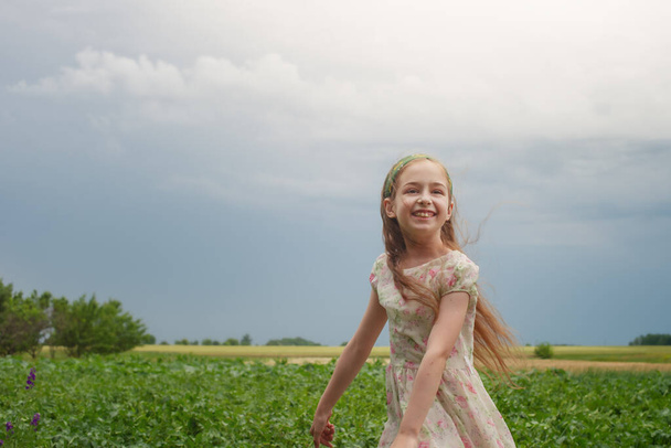 The joy of a child. A little girl in a flower dress against the background of rural nature. - Фото, изображение