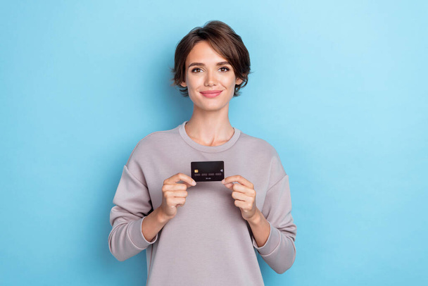 Portrait of gorgeous good mood woman bob hairdo dressed gray sweatshirt hold credit card online purchase isolated on blue color background. - Foto, Imagen
