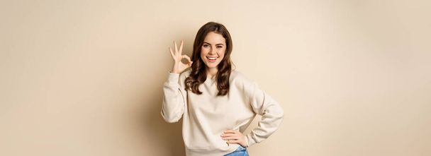 Excellent. Smiling beautiful woman showing okay, ok zero sign, approve smth good, praising and complimenting, beige background. - Foto, Imagen