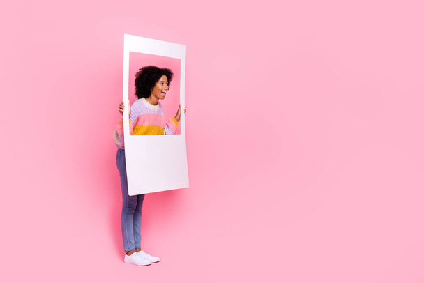 Full length photo of impressed excited girl perming coiffure knit sweater hold frame look empty space isolated on pink color background. - 写真・画像