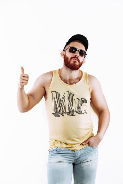 Hipster redhead bearded man in cap in sunglasses in summer clothes showing thumb up on white background while looking at camera  - Photo, Image