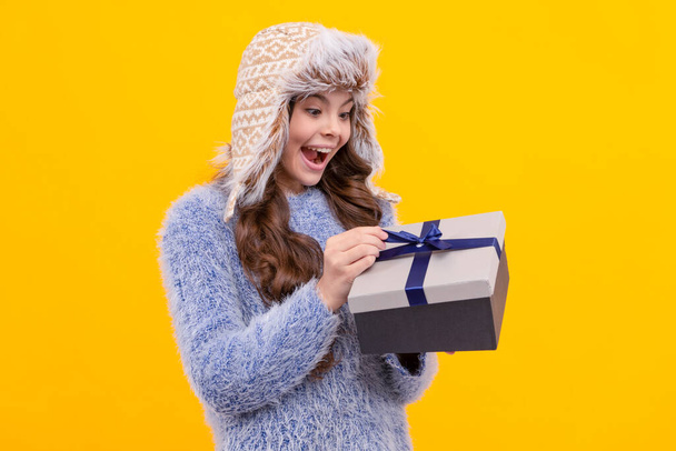 happy kid open purchase in hat. boxing day. teen girl in knitwear on yellow background. child buy gift. black friday discount. winter shopping sale. birthday present box. christmas season. - Photo, Image