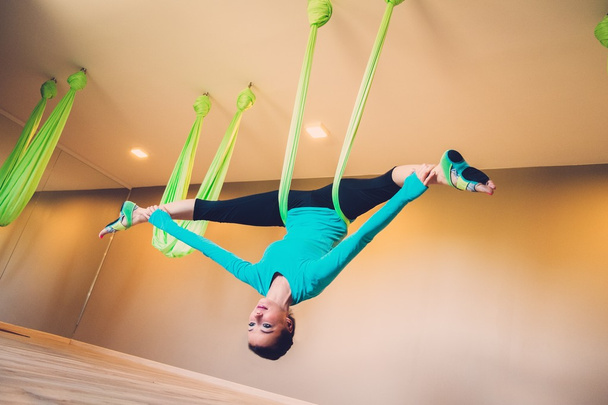 Jonge vrouw uitvoeren van anti-zwaartekracht yoga oefening - Foto, afbeelding