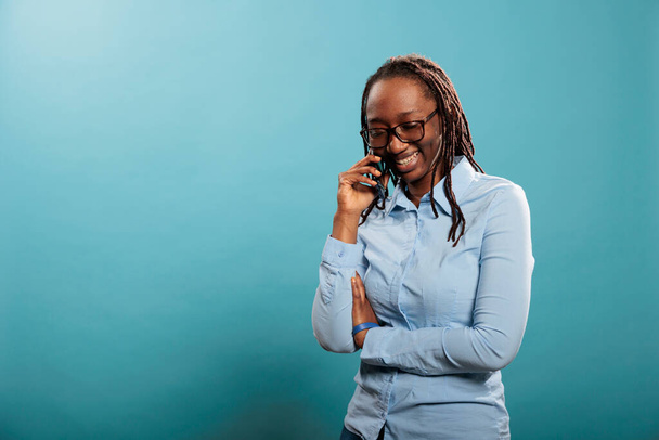 Happy joyful young woman smiling heartily while having a phone call conversation on blue background. Cheerful adult person talking with friend on touchscreen cellphone device. - Fotoğraf, Görsel