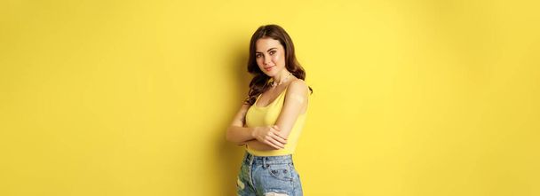 Vaccination campaign concept. Cute smiling young woman after getting vaccinated, standing with patch on her shoulder and looking healthy and happy, yellow background. - Φωτογραφία, εικόνα
