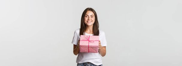 Surprised happy birthday girl receiving wrapped gift, white background. - Photo, Image