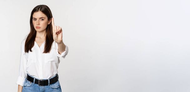 Serious woman showing taboo, stop gesture, shaking finger in disapproval, disagree, forbidding something, standing over white background. - Фото, изображение
