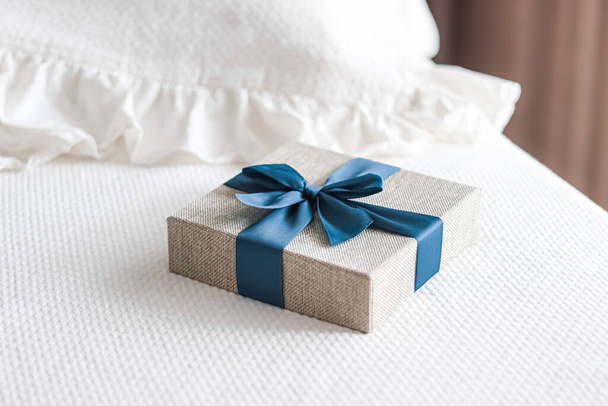 Holiday present and luxury online shopping delivery, wrapped linen gift box with blue ribbon on bed in bedroom, chic countryside style, close-up - Foto, imagen