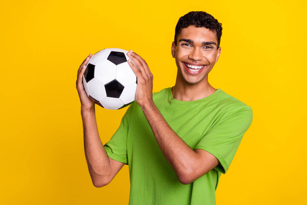 Portrait of satisfied excited man beaming smile arms hold football isolated on yellow color background. - Fotó, kép