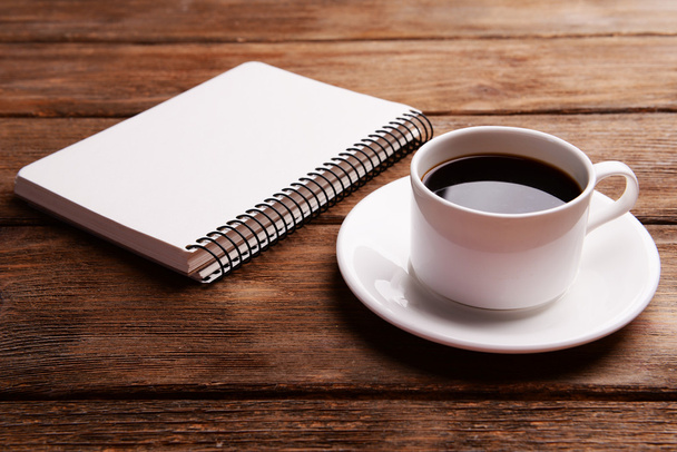 Cup of coffee on saucer with notebook on wooden table background - Fotó, kép