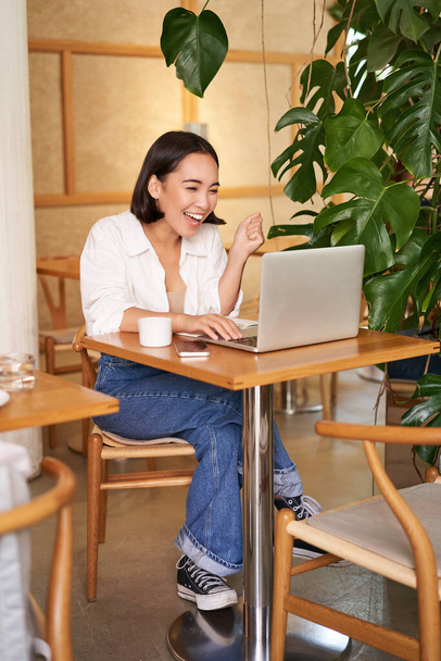 Excitada menina asiática encontrou algo on-line, olhando para a tela do laptop com rosto surpreso, surpreso, sentado no café. - Foto, Imagem