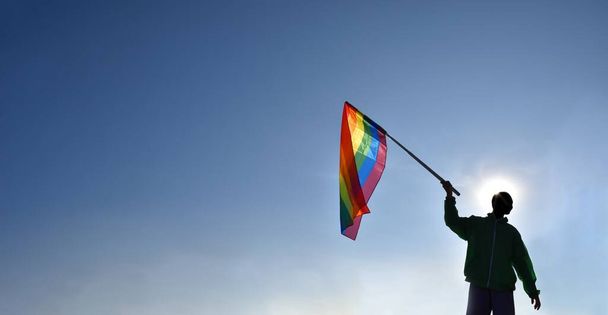 Rainbow flag, LGBT simbol, holding in hands of boy against clear bluesky background, soft and  selective focus, concept for LGBT celebration in pride month, June, around the world, copy space. - Photo, Image