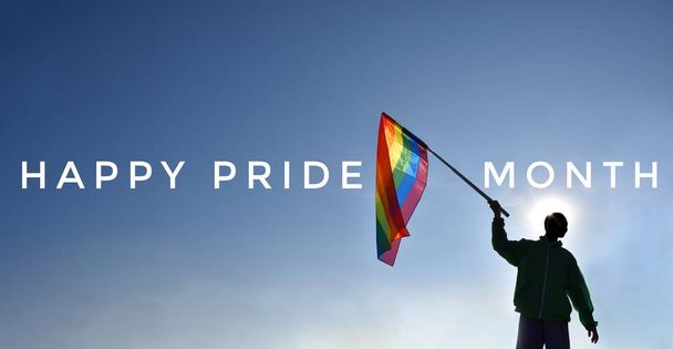 'Happy Pride Month' на голубом и радужном флаге, держащемся в руке на фоне заката, концепция для длительных празднований в месяце гордости, июнь, - Фото, изображение