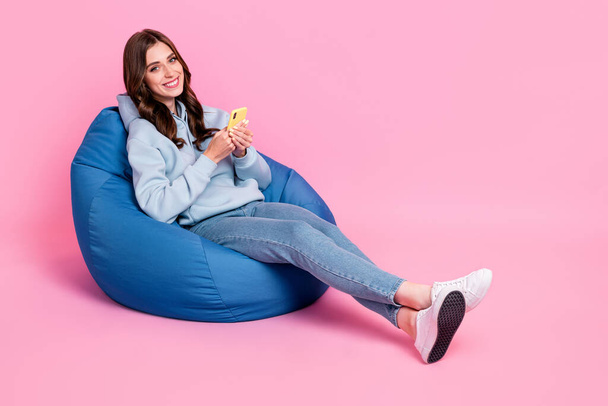 Full length photo of gorgeous cheerful person sit cozy bag use telephone isolated on pink color background. - Foto, Imagen