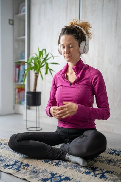 una mujer adulta caucásica milenaria usando auriculares y computadora portátil para la meditación guiada en línea practicando mindfulness yoga con los ojos cerrados en el suelo en casa personas reales copiar espacio - Foto, imagen