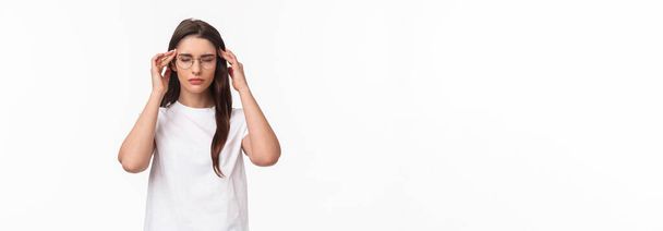 Waist-up portrait of attractive young woman trying get ready, massaging temples with closed eyes as relaxing, ease the pain, thinking rational, put effort into making up plan, white background. - Photo, Image