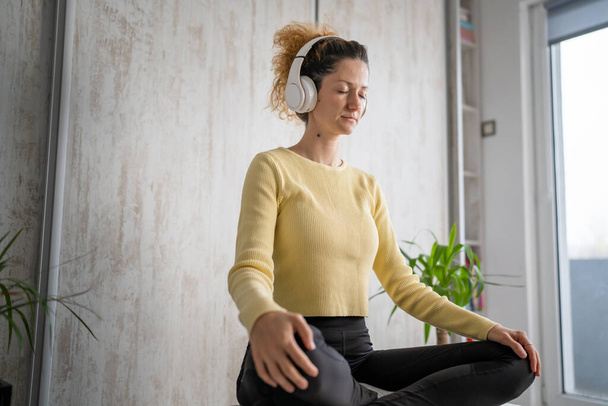 una mujer adulta caucásica milenaria usando auriculares para la meditación guiada en línea practicando mindfulness yoga con los ojos cerrados en el suelo en casa personas reales copiar espacio concepto de autocuidado - Foto, imagen