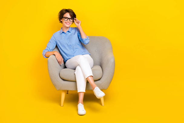 Full length photo of confident cute lady wear blue shirt arms spectacles relaxing couch empty space isolated yellow color background. - Foto, Bild