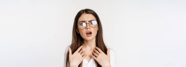 Offended and upset young woman in glasses, beeing jealous or disappointed, feeling hurt, grimacing and sulking, standing confused over white background. - Photo, image