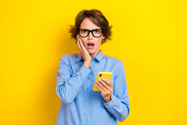 Closeup photo of young impressed young student college information hold phone deadline touch cheeks confused isolated on yellow color background. - Fotografie, Obrázek