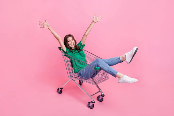 Full length photo of overjoyed cute lady wear stylish clothes sit trolley raise hand rejoice good mood isolated on pink color background. - 写真・画像