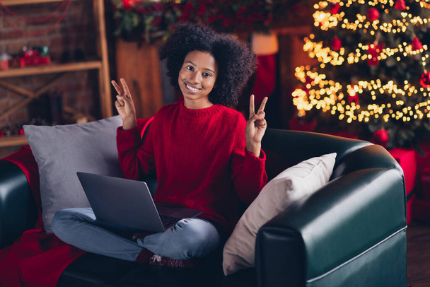Full body portrait of beautiful cute positive girl sit sofa use wireless netbook show v-sign enjoy festive time indoors. - Photo, image