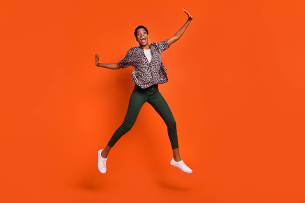 Full length body size view of attractive cheerful trendy girl jumping having fun isolated over vivid orange color background. - Foto, Imagem