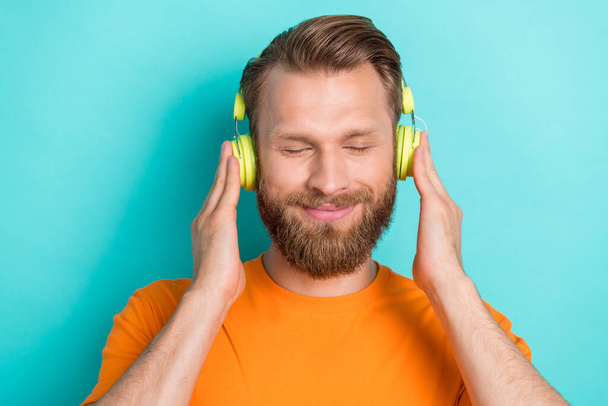 Photo of funky beard guy listen music wear orange t-shirt isolated on teal color backgroiund. - Photo, Image